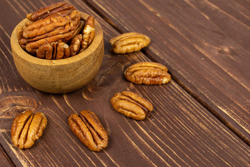 Lot of whole dry brown pecan nut in tiny wooden bowl on brown wood