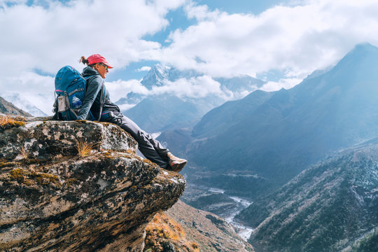 Young hiker backpacker female sitting on cliff edge and enjoying the Imja Khola valley during high altitude Everest Base Camp (EBC) trekking route near Phortse, Nepal. Active vacations concept image.