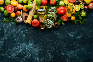 Raw green pasta with tomatoes, oil and parsley on a black stone background. Italian traditional cuisine. Fresh vegetables. Top view. Free space for your text.