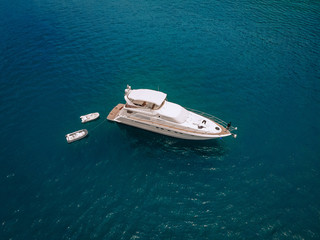Drone shot of the beautiful white yacht in the warm blue sea; wealth concept.