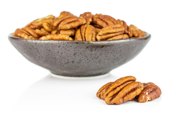 Lot of whole dry brown pecan nut in dark ceramic bowl isolated on white background