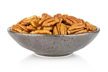 Lot of whole dry brown pecan nut in dark ceramic bowl isolated on white background