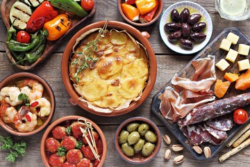 Spanish tapas. Traditional mediterranean appetizer table concept included tortilla, grilled vegetables, meatballs, garlic king prawns,olives and cured meat. - obrazy, fototapety, plakaty