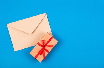 Top view of simple gift box decorated with red bow ribbon and craft envelope on blue background. Flat lay. Minimal concept. .