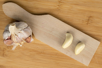 Group of one whole two pieces of aromatic white garlic on wooden cutting board flatlay on light wood