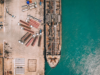 Drone view of the oil tanker at the quay, pumping fuel into numerous petrol trucks through gas pipes; technology concept.