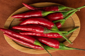 Lot of whole hot red chili on round bamboo coaster flatlay on cognac leather