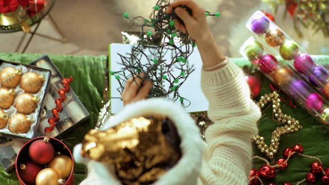 Holiday season. Upper view of unhappy trendy female in sparkle gold sequin santa hat sitting on divan in the modern living room at Christmas holding tangled christmas lights. PRORes 422 codec.