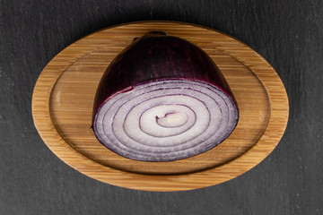 One half of tasty onion red on round bamboo coaster flatlay on grey stone