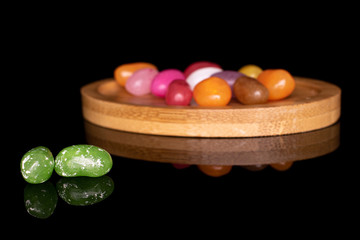 Lot of whole jelly bean candy green in focus on round bamboo coaster isolated on black glass