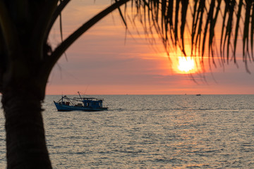 Vietnam, Phu Quoc island, sunset on sea. view through the palm leaves in the sun. ships sail on the...
