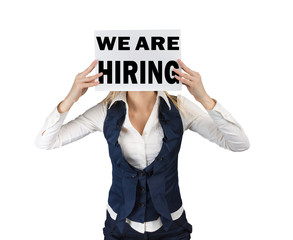 White woman holds sheet of paper ad at head level with text we are hiring