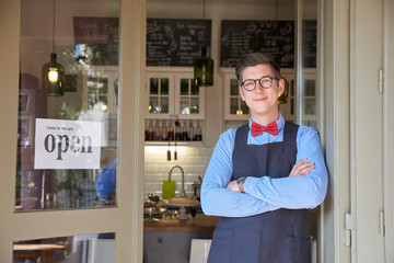 Fototapeta premium Small business owner standing in the cafe entrance with open sign while wating for guest