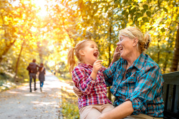 Fototapeta premium Smiling grandmother and granddaughter enjoy spending time together in autumn park