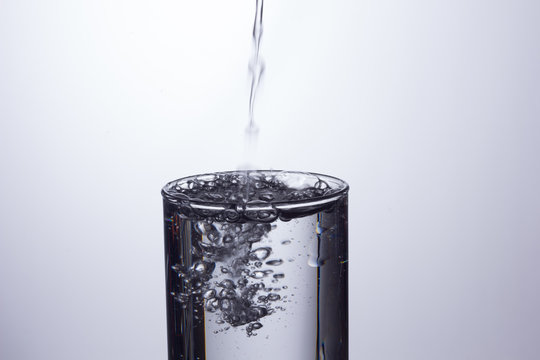 Agua entrando en un recipiente transparente de crital o pl&aacute;stico; agua salpicando 