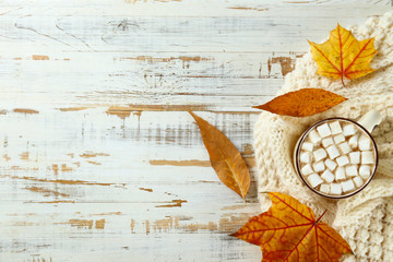 Big cup of cacao hot beverage with bunch of marshmallows on top and dry autumn leaves over grunged...