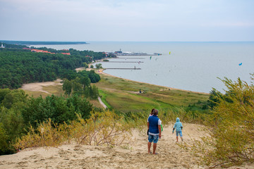 Fototapeta na wymiar Panoramic view from sand dunes in Nida, Klaipeda, Lithuania, Europe. Curonian Spit and Curonian Lagoon, Nida harbour. Baltic Dunes. Unesco heritage. Tourists walking on the dunes