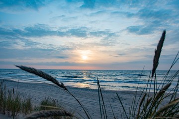 Beautiful sunset on the Baltic Sea with reeds in the foreground, waves and reflections on the water
