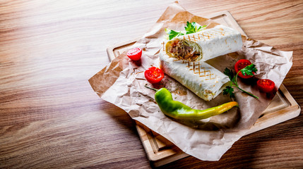 Shawarma with meat and vegetables lies on wooden table background