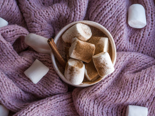 Obraz na płótnie Canvas Cozy mood lifestile, still life concept. Mug of aromatic cacao, sweater and cinnamon on pink knitted sweaters as background. Traditional winter or autumn hot drink at home. Top view, flat lay, closeup
