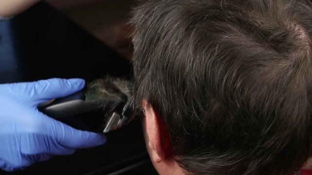 Barber cuts the hair of the man with electric hair clippers