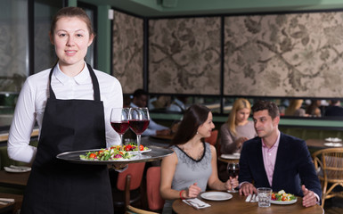 Polite waitress holding tray with dishes