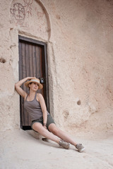 Tourist girl in straw hat and shorts sit on near cave house door in Gereme National Park, Open air museum looking on Fabulous Cappadocia mountains landscapes Turkey/ Travel and adventur concept