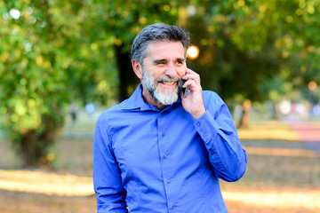 Handsome man with a seductive smile in park, working on cell phone. Senior man using tablet computer in park. Business, technology and people concept - Senior businessman with tablet pc computer