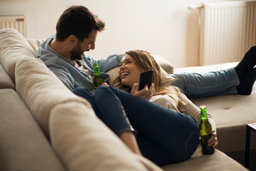 Obraz premium Young happy couple drinking beer and listening music at home