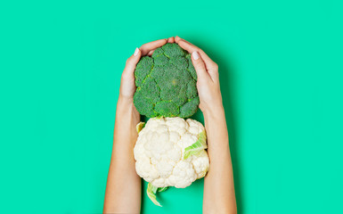 Female hand holding broccoli on green background.