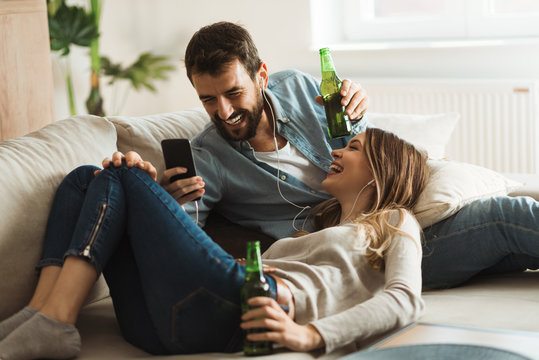 Young couple enjoying in MP3 music while drinking beer at home