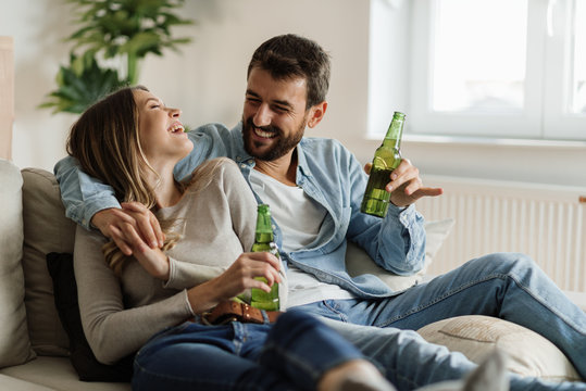 Young Happy Couple Communicating While Sitting On The Sofa And Drinking Beer