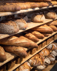 Round breads and long french loaves on shelves. Baked goods.