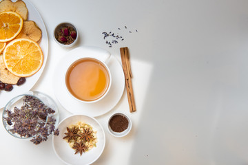 a white mug on a white table with herbal tea and herbal ingredients laid out on the table. Concept on the topic of herbal treatment for colds and flu in autumn. Top view