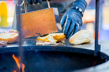 gloved hand collects a patty, cheese and vegetables on a burger roll. Ready order