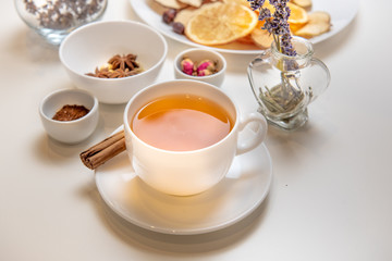 a white mug on a white table with herbal tea and herbal ingredients laid out on the table. Concept on the topic of herbal treatment for colds and flu in autumn. Top view