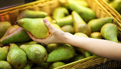 Female hand chooses pear in the store. Concept of healthy food, bio, vegetarian, diet.