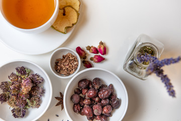 a white mug on a white table with herbal tea and herbal ingredients laid out on the table. Concept on the topic of herbal treatment for colds and flu in autumn. Top view