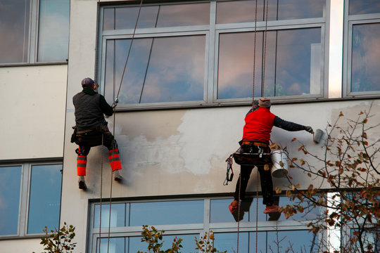 two industrial climbers paint the facade of a house hanging on ropes