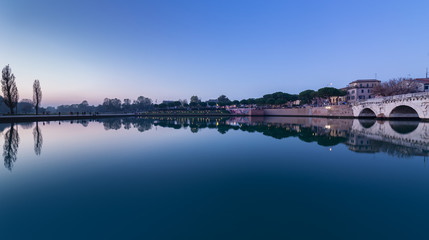 Rimini city landscape on riverside. Tiberius bridge and city park at sunset. Twilight view - 299177640