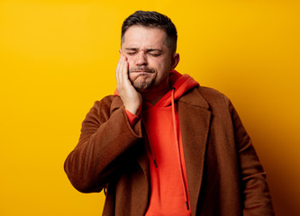 Fototapeta premium Angry man in coat with tooth pain on yellow background