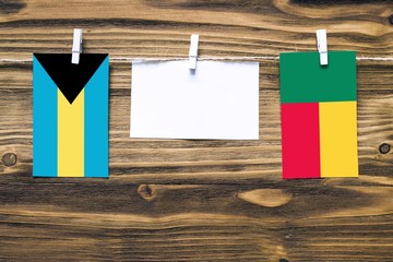 Hanging flags of Bahamas and Benin attached to rope with clothes pins with copy space on white note paper on wooden background.Diplomatic relations between countries.