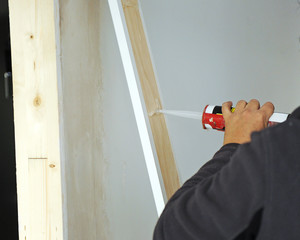 Carpenter sticking the white frame of a sliding door with a silicone gun