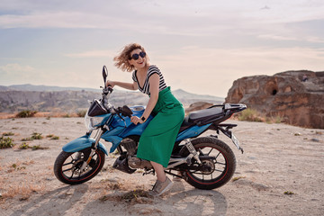 Fototapeta na wymiar Young slim pretty happy fashion woman riding a bike. Girl biker racer motorbike on the desert. Outdoor lifestyle portrait. National park Anatolia, Cappadocia, Turkey. The feeling of complete freedom