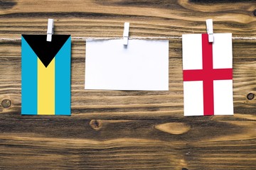 Hanging flags of Bahamas and England attached to rope with clothes pins with copy space on white note paper on wooden background.Diplomatic relations between countries.