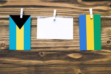 Hanging flags of Bahamas and Gabon attached to rope with clothes pins with copy space on white note...