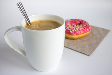 A large white cappuccino Cup and a frosting doughnut
