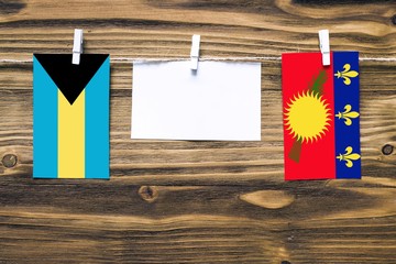 Hanging flags of Bahamas and Guadeloupe attached to rope with clothes pins with copy space on white note paper on wooden background.Diplomatic relations between countries.