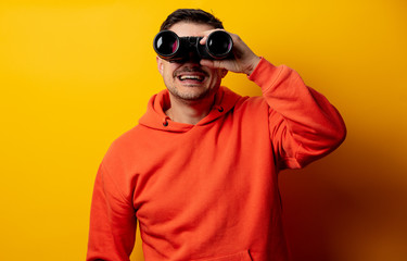 Handsome man with binocular on yellow background