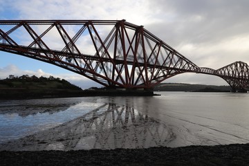 Firth of Forth at low tide with rail bridge casting reflection in water
